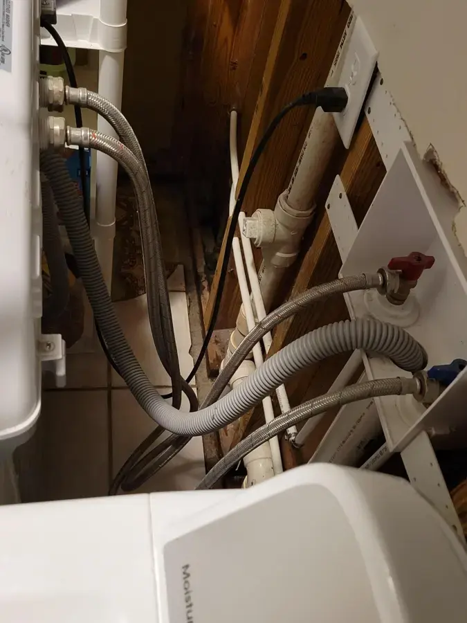 Washer supply hoses and valves behind a laundry machine with a water-damaged wall opened in Plant City
