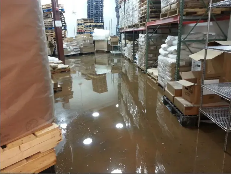 Standing water across a warehouse floor between pallets and racks